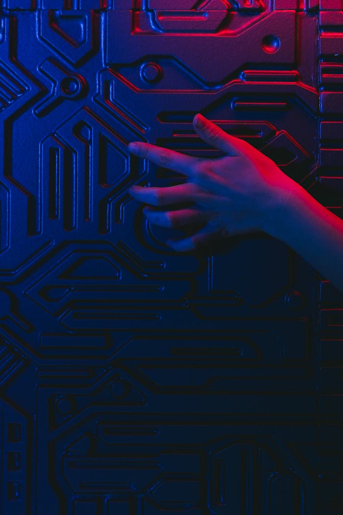 Close-up of a human hand touching a circuit board with blue and red neon lighting.